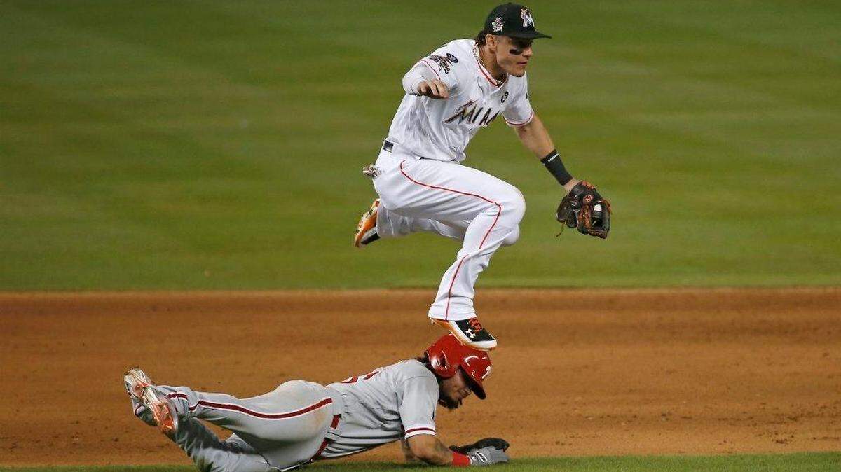 El tercera base de los Marlins Derek Dietrich salta sobre el torpedero de los Filis Freddy Galvis en una jugada del partido celebrado el 31 de agosto del 2017 en Miami.