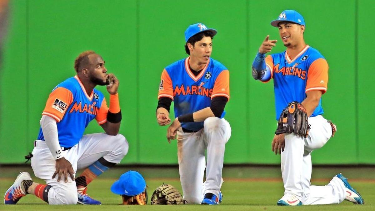 MARCELL OZUNA (i), Christian Yelich (c), y Giancarlo Stanton conversan en la pradera central durante una pausa de un juego el 25 de agosto.