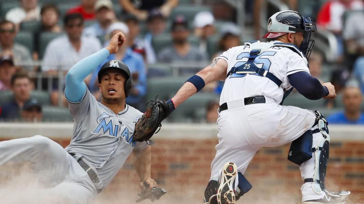 Giancarlo Stanton (27), de los Marlins, anota una carrera ante Tyler Flowers (25), de los Bravos, el sábado.