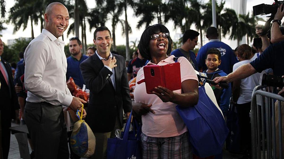 Derek Jeter, director ejecutivo de los Marlins, entrega un pavo a Joann Brady, quien inmortaliza el momento ante el alcalde de Miami Francis Suárez (centro) en el evento anual por Thankgivings realizado este viernes 7 en el Marlins Park.