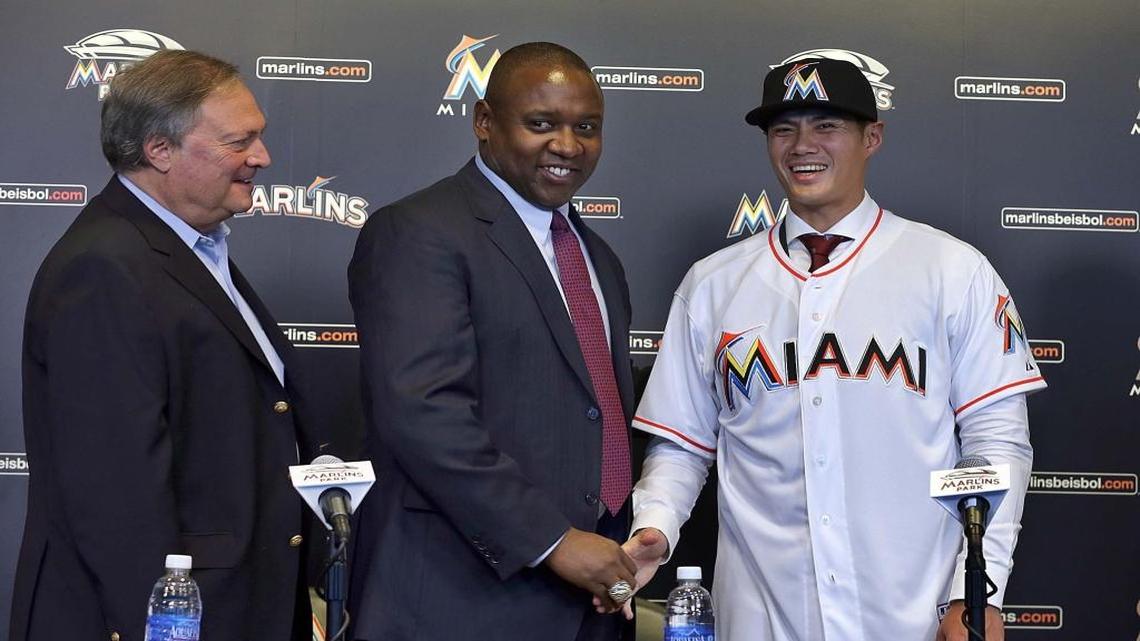 El pitcher de los Marlins Wei-Yin Chen (der.) estrecha la mano con Michael Hill, presidente de operaciones de béisbol del club, en la presentación oficial del lanzador ante los medios de prensa, el martes en el estadio Marlins Park, de Miami. A la izquierda el dueño del equipo Jeffrey Loria.