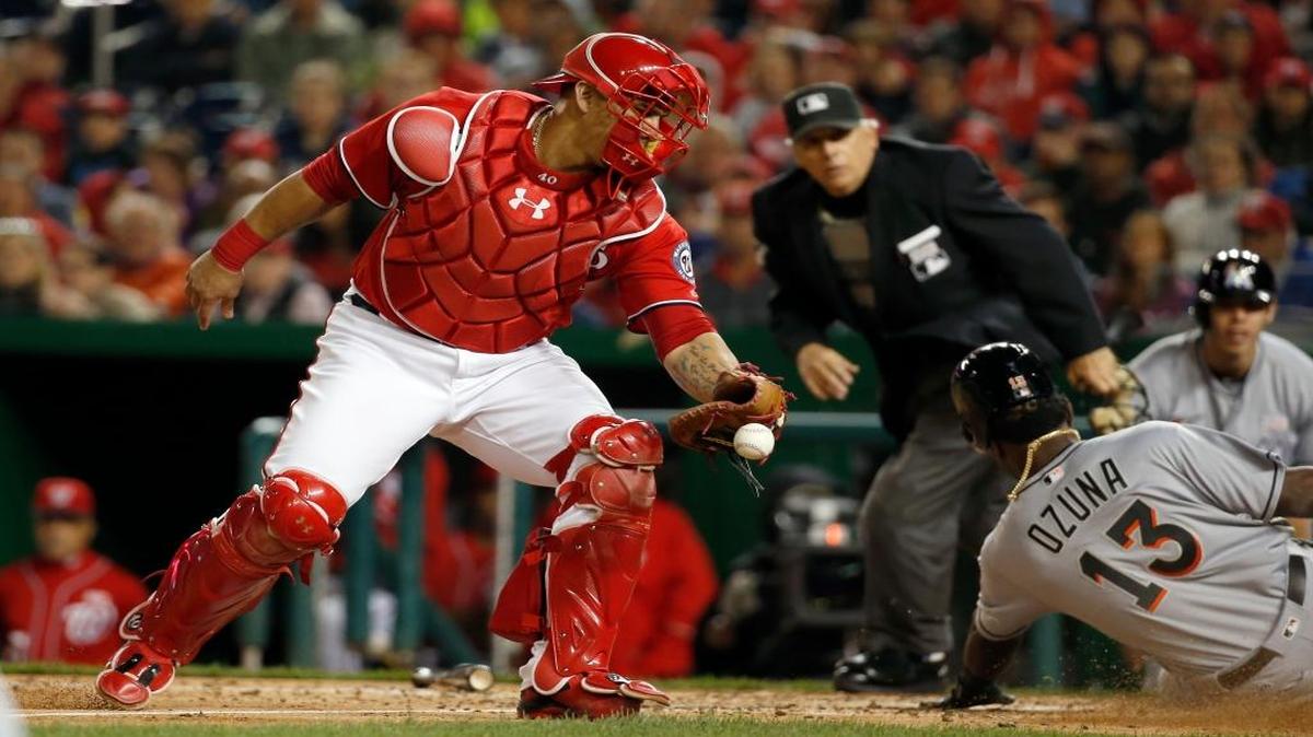 El receptor Wilson Ramos (izq.) no puede atrapar el tiro y Marcell Ozuna, de los Marlins, anota una carrera, en el quinto inning del segundo juego en la doble cartelera contra los Nacionales, el sábado 14 de mayo del 2016, en Washington.
