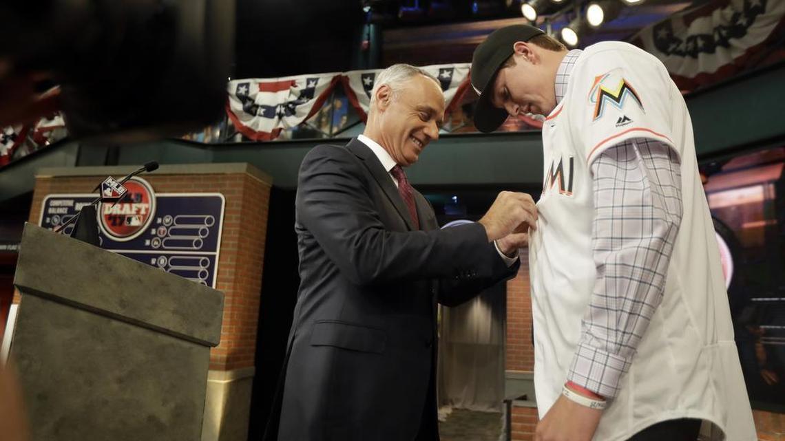El comisionado de Grandes Ligas Rob Manfred (izq.) le abotona la camiseta de los Marlins a Trevor Rogers durante la ceremonia del draf, celebrada el 12 de junio del 2017 en Secaucus, Nueva Jersey.