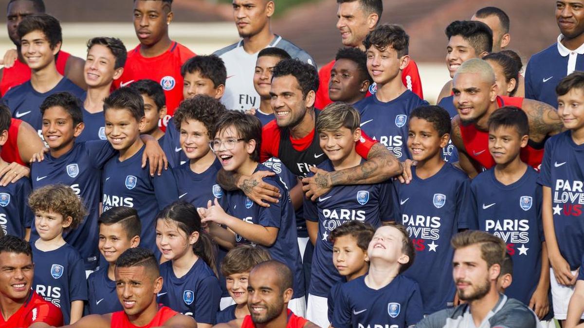 Los Jugadores del Paris Saint-Germain posan junto a chicos y chicas de la academia del club francés en Miami en la práctica en Barry University, el domingo 16 de julio del 2017. En el centro el brasileño Dani Alves abraza a dos de los aspirantes a estrellas.