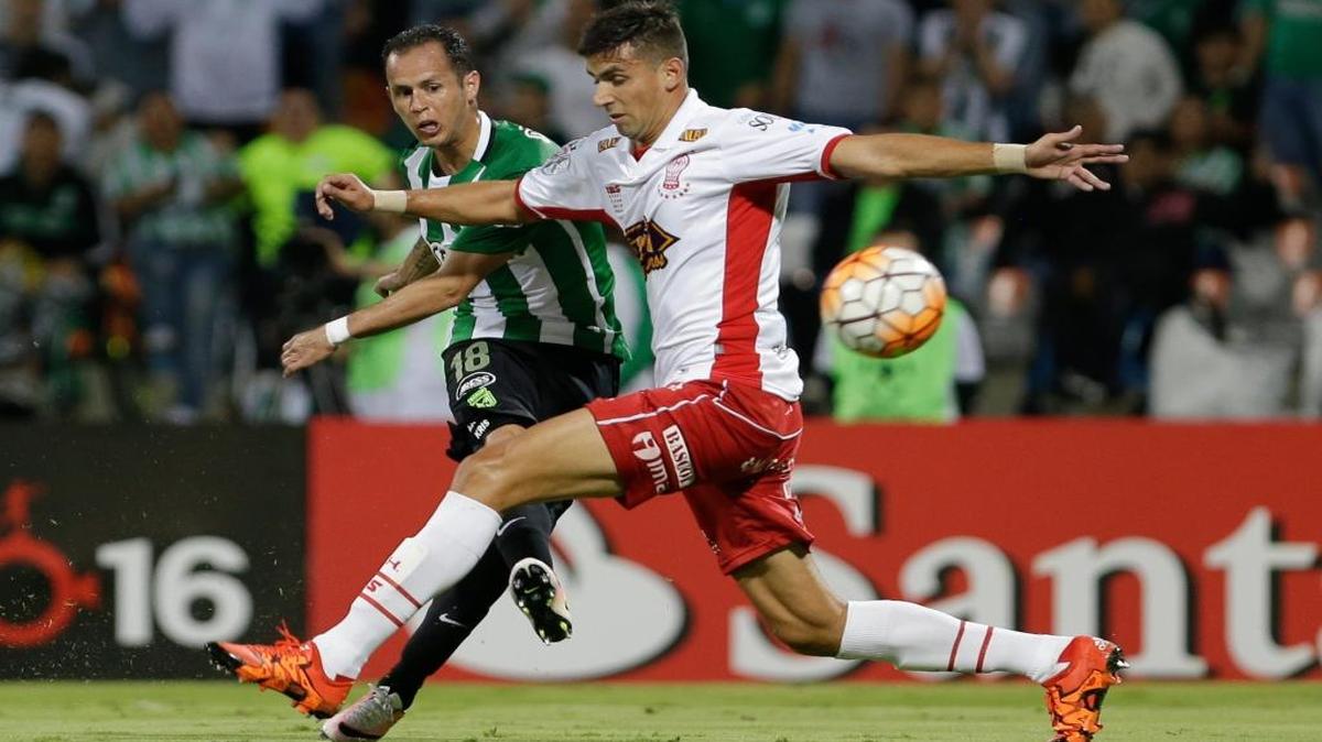 El venezolano Alejandro Guerra, del Atlético Nacional, dispara sobre la marcación de Mario Risso para anotar uno de sus goles contra Huracán de Argentina, en la Copa Libertadores, en Medellín, Colombia, el martes 3 de mayo del 2016.