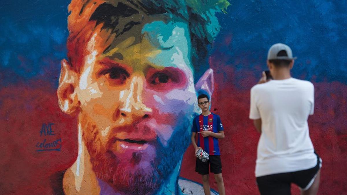 Un joven posa junto a un mural del astro del fútbol Lionel Messi en Barcelona, España.