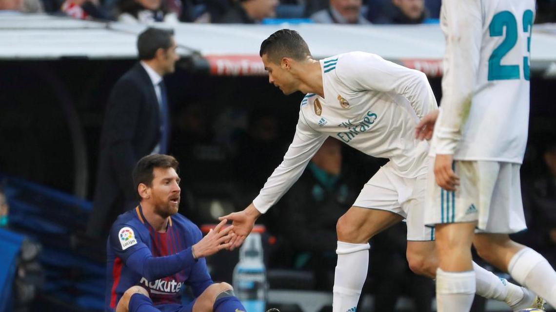 El delantero portugués del Real Madrid, Cristiano Ronaldo (centro), ayuda a levantarse al delantero argentino del Barcelona, Lionel Messi durante el partido efectuado el 23 de diciembre de 2017 en el estadio Santiago Bernabéu, de Madrid.