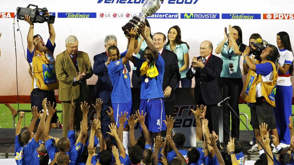 Jugadores brasileños Gilberto Silva (izq.) y Juan levantan el trofeo después que Brasil ganó el partido final de la Copa América 2007 contra Argentina en el estadio Pachencho Romero en Maracaibo, Venezuela, 15 de julio de 2007. Entre los jugadores que levantan el trofeo y una azafata aparece el paraguayo Nicolás Leoz, acusado de recibir millonarios sobornos cuando estaba al frente de la Confederación Sudamericana de Fútbol.
