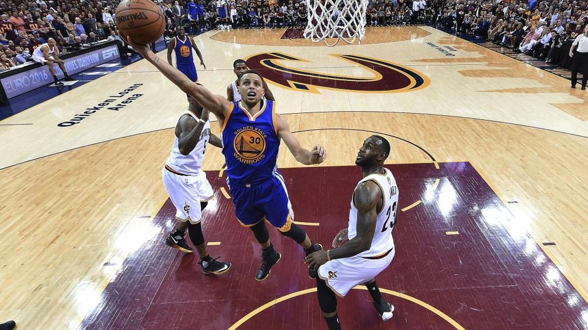 El armador Stephen Curry (30), quien lideró la ofensiva de los Warriors, tira al aro ante el astro de los Cavaliers LeBron James (23) en el Juego $ el viernes en Cleveland.