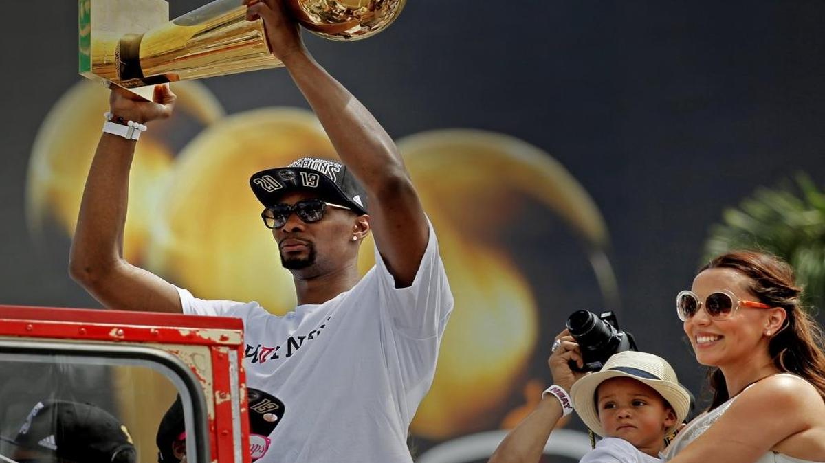 Chris Bosh levanta el trofeo de campeón de la NBA, que ganó con el Heat, en el desfile en junio del 2013. Al lado su hija Trinity y su esposa Adrienne Williams Bosh.