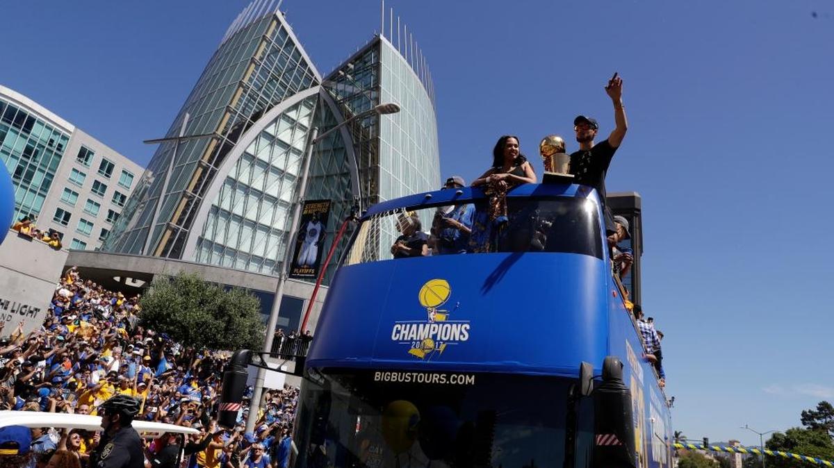 Stephen Curry, portando el trofeo de campeones de la NBA conquistado por sus Warriors, saluda a los aficionados durante la parada de celebración de este jueves en Oakland.