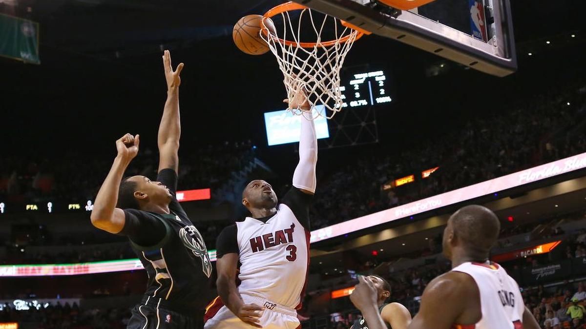 Dwyane Wade (centro) trata de anotar la canasta ante la marca de John Henson (izq.), en el partido entre el Heat y los Bucks el 19 de enero del 2016 en Miami.