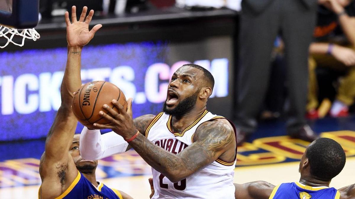 
LeBron James (centro) penetra al aro por los Cavaliers ante la marca de Andre Iguodala (izq.), de los Warriors, en el sexto juego de la Final de la NBA el 16 de junio del 2015.
