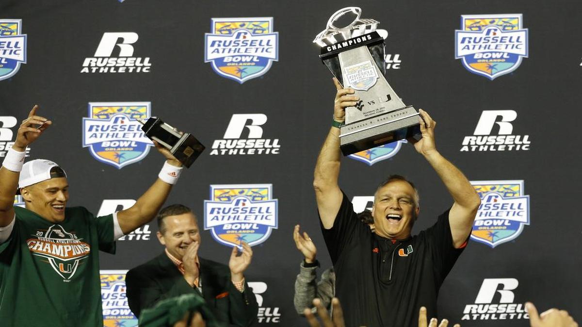 El coach de los Huracanes Mark Richt levanta el trofeo de campeones que ganó el equipo de Miami tras derrotar a West Virginia en el Russell Athletic Bowl, el 28 de diciembre del 2016 en Orlando, Florida.