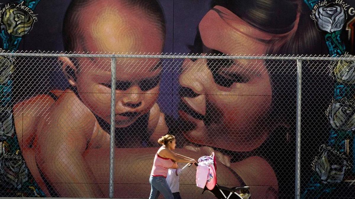 Una mujer camina frente a un mural que representa a una madre hispana en MacArthur Park Primary Center School en Los Angeles.