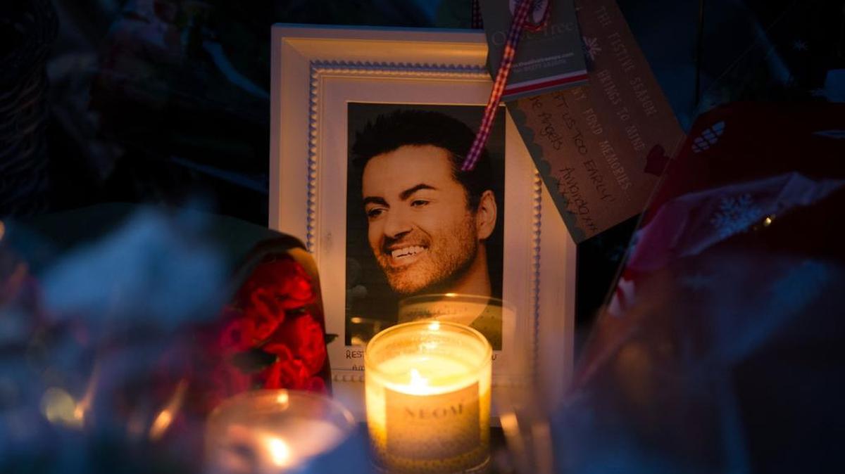 Un retrato del cantante británico George Michael es iluminado por una vela entre flores y mensajes dejados en homenaje fuera de la casa del cantante, en la aldea de Goring, sur de Inglaterra, el 27 de diciembre de 2016.