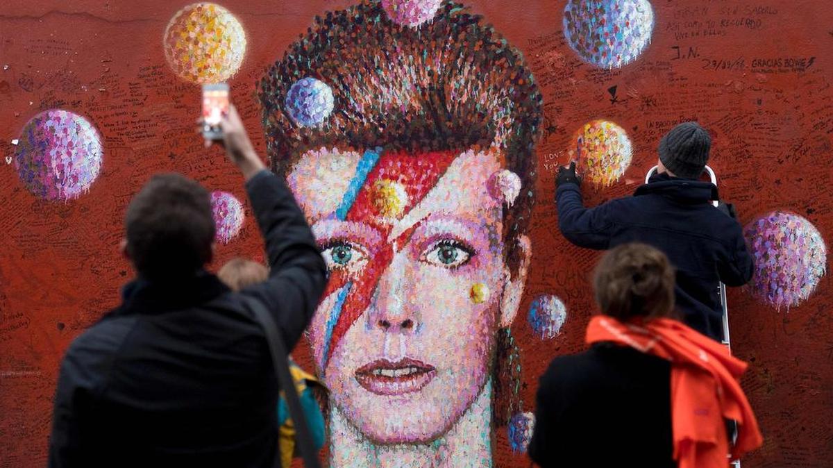 Transeúntes paran para observar y fotografiar al artista callejero australiano James Cochran, también conocido como Jimmy C, que retoca el mural del músico británico David Bowie en Brixton, al sur de Londres el 7 diciembre de 2016.