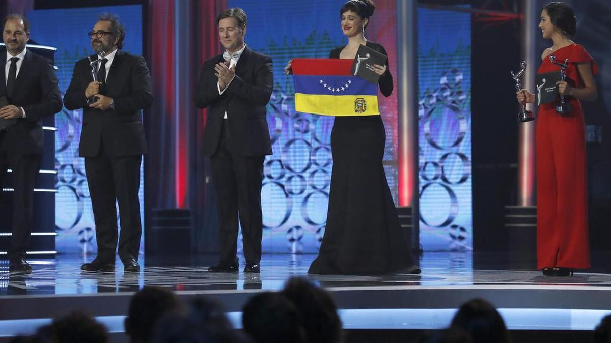La actriz, directora y escritora venezolana Pakriti Maduro muestra una bandera de su pais durante la ceremonia de entrega de los IV Premios Platino del Cine Iberoamericano celebrada esta noche en la Caja Mágica, en Madrid.A la izquierda, el presentador de la gala Carlos Latre.