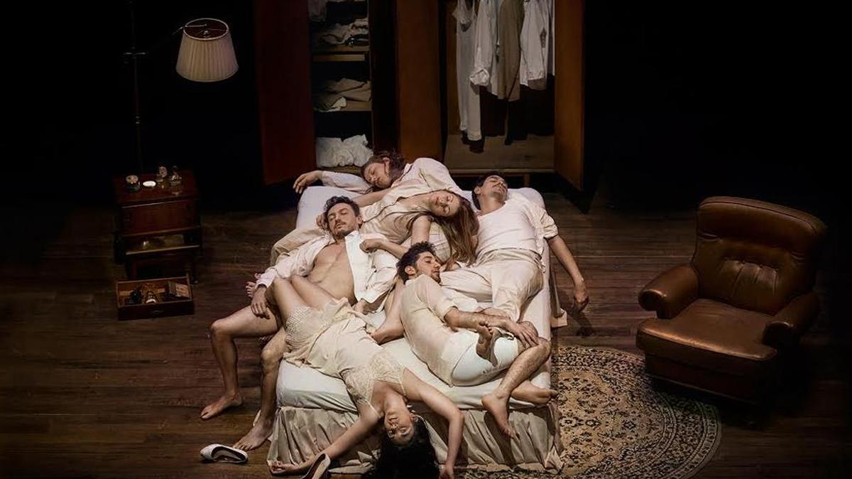 La obra comienza con una cama al centro donde seis cuerpos entrelazados parecen reposar.