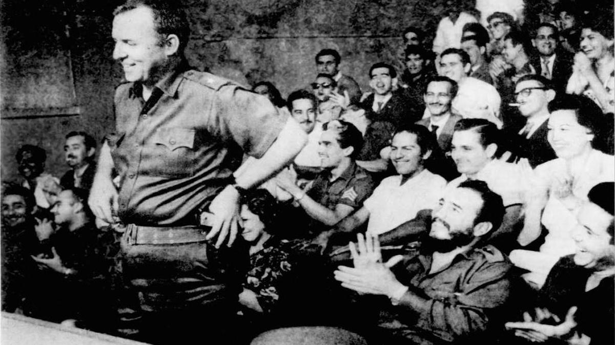 William Morgan (al frente) habla en una reunión al principio de la Revolución. Detrás, Fidel Castro, sentado entre la audiencia, aplaude.