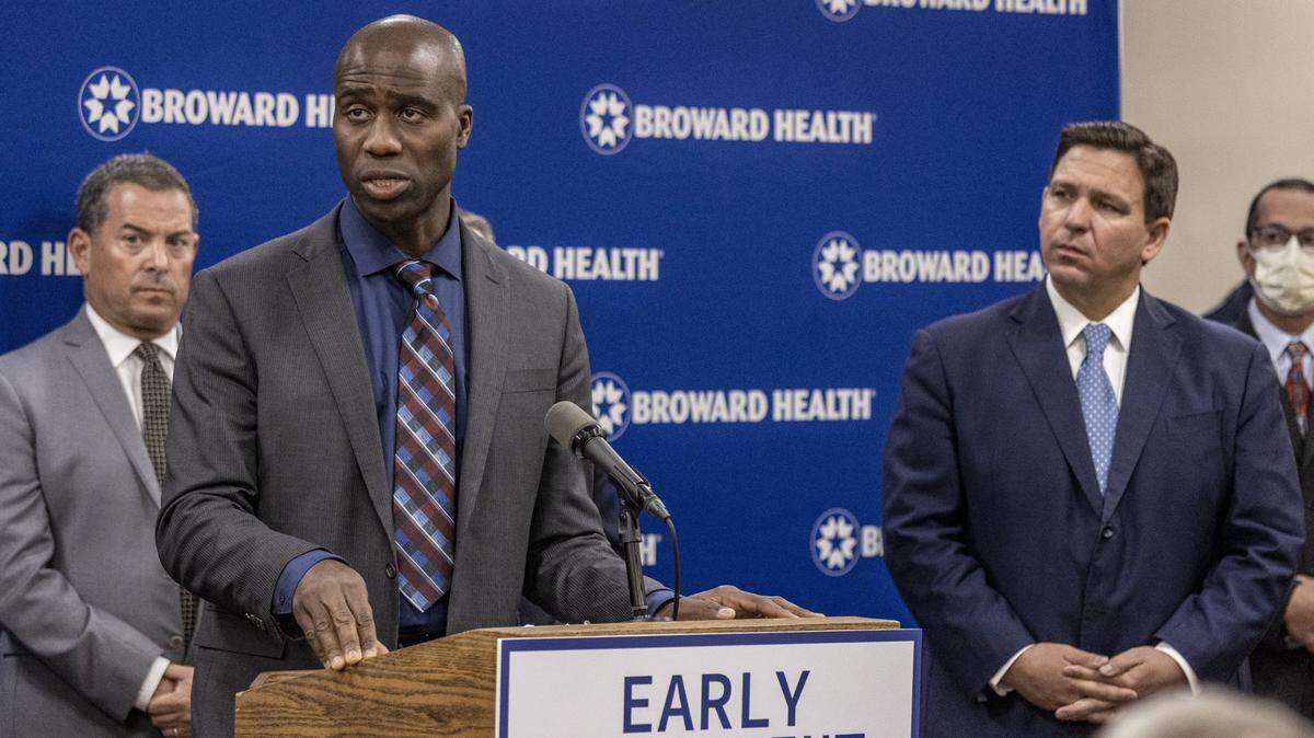 Dr. Joseph Ladapo, left, is Florida’s surgeon general. Gov. Ron DeSantis, right, appointed him to the post in 2021. Ladapo is urging local governments to stop adding fluoride to water supplies, which public health groups say is key to reducing cavities, especially for low-income families.