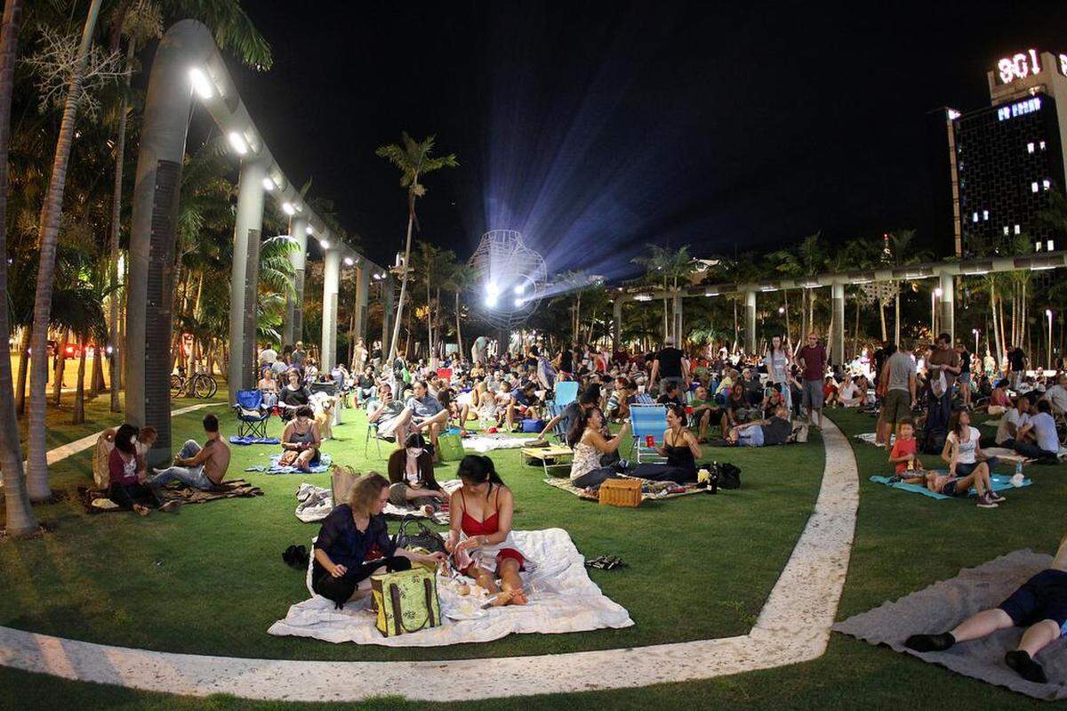 Gente se acomoda en sus mantas y sillas durante la proyección de una película en el Miami Beach SoundScape ExoStage.