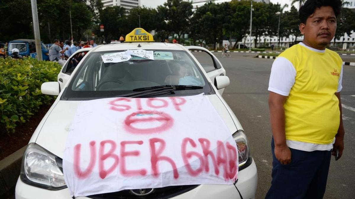 Un conductor de taxi posa junto a su vehículo con un letrero contra Uber, en Indonesia, la semana pasada. En Argentina, el sindicato de taxistas también se opone a este servicio.