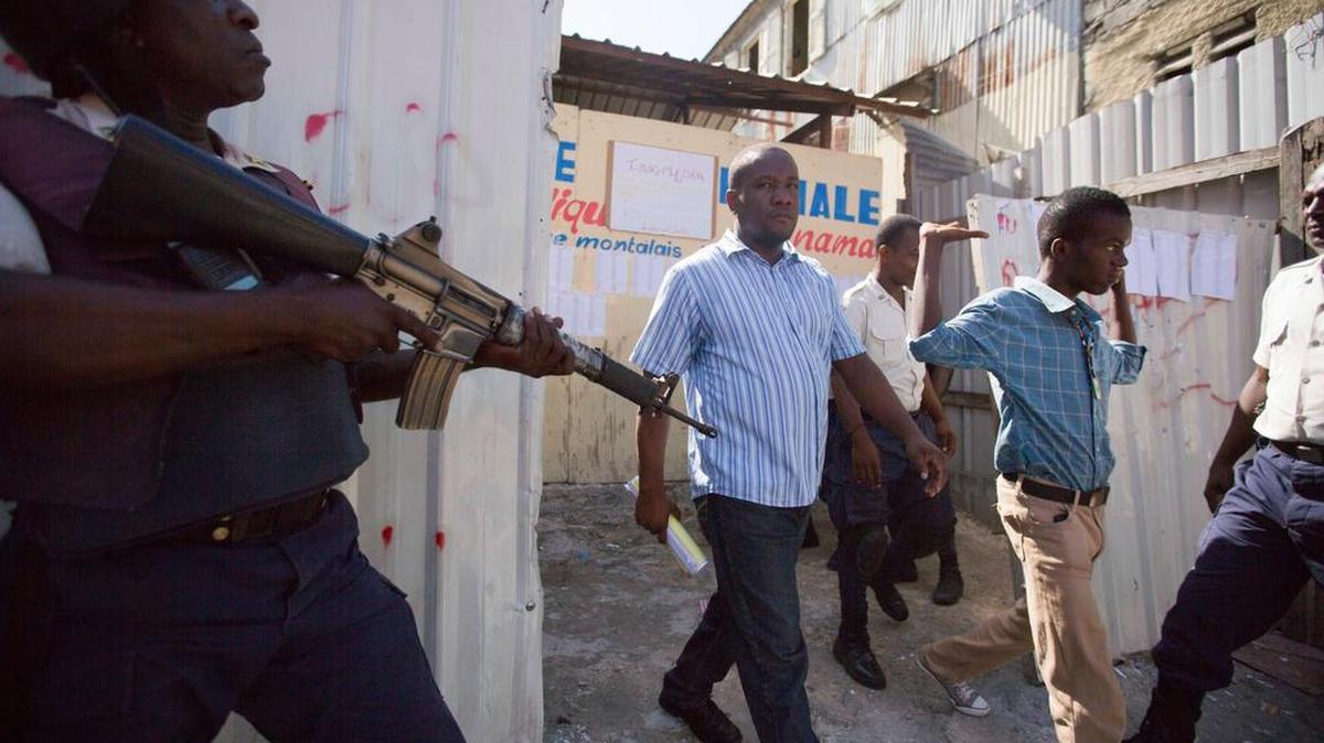 
Haitianos son escoltados el domingo fuera de un centro de votación en Puerto Príncipe, cerrado debido a la violencia durante las elecciones parlamentarias. Haití realizó los primeros comicios legislativos desde el 2011. 
