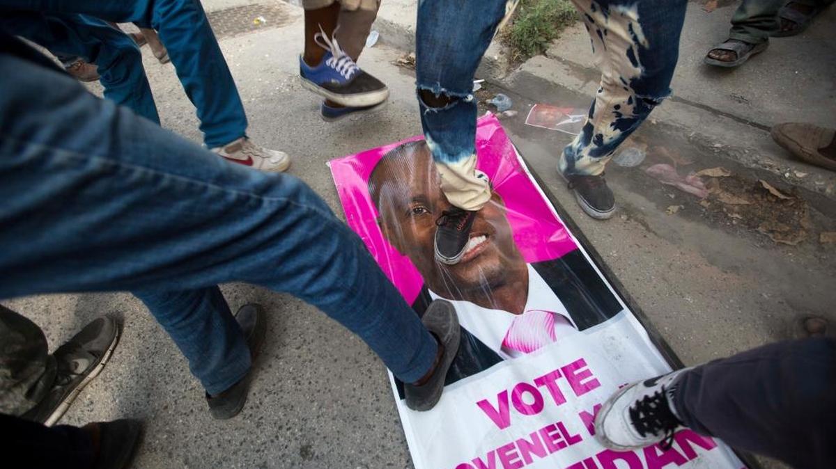 Manifestantes pisan una pancarta del oficialista Jovenel Moise, durante una protesta contra los resultados preliminares de la primera vuelta de las elecciones.