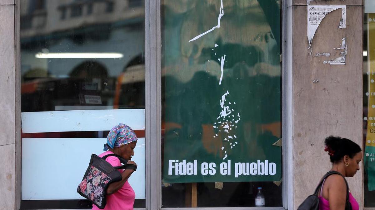 Fotografía del 3 de marzo de 2017, donde se observa a dos personas caminando junto a un cartel alusivo al fallecido líder cubano Fidel Castro en La Habana (Cuba).