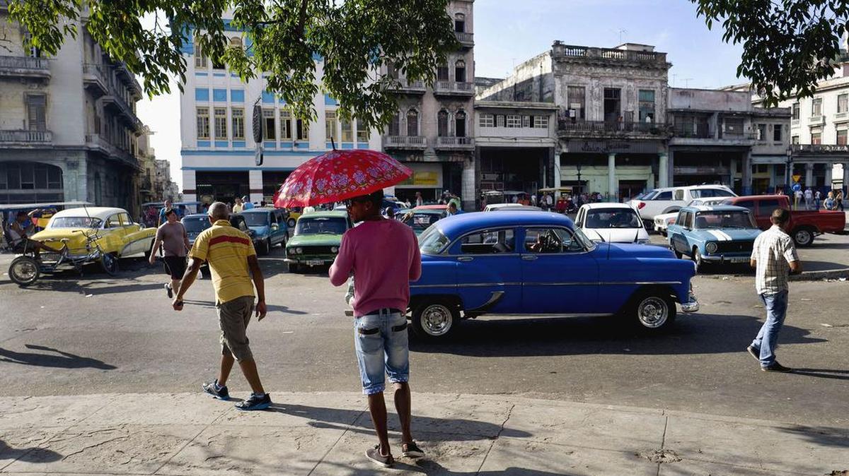 Un hombre sostiene un paraguas mientras que está parado en una acera en La Habana, Cuba. Foto de archivo.
