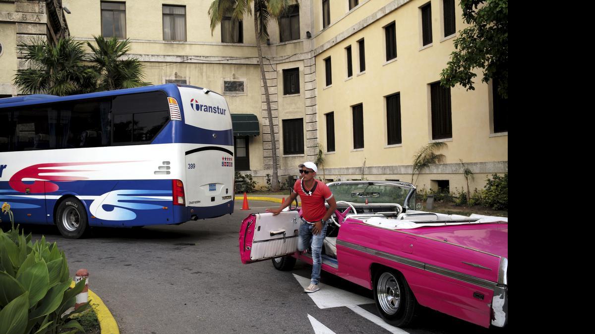 
Un hombre se baja de un auto convertible en La Habana detrás de un autobús de turismo.
