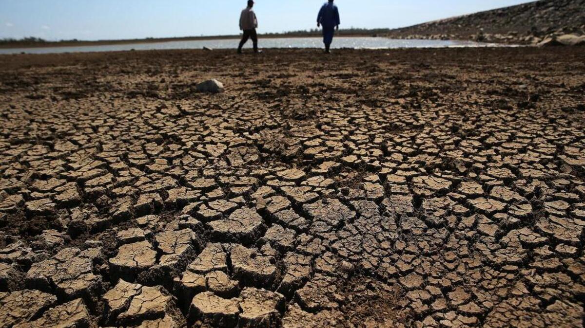 Fotografía tomada el 3 de abril de 2017, que muestra a dos obreros que caminan sobre la tierra agrietada del fondo de la presa “Sábanas Blancas”, que se encuentra por debajo del mínimo de su capacidad de embalse en la provincia de Ciego de Ávila (Cuba).