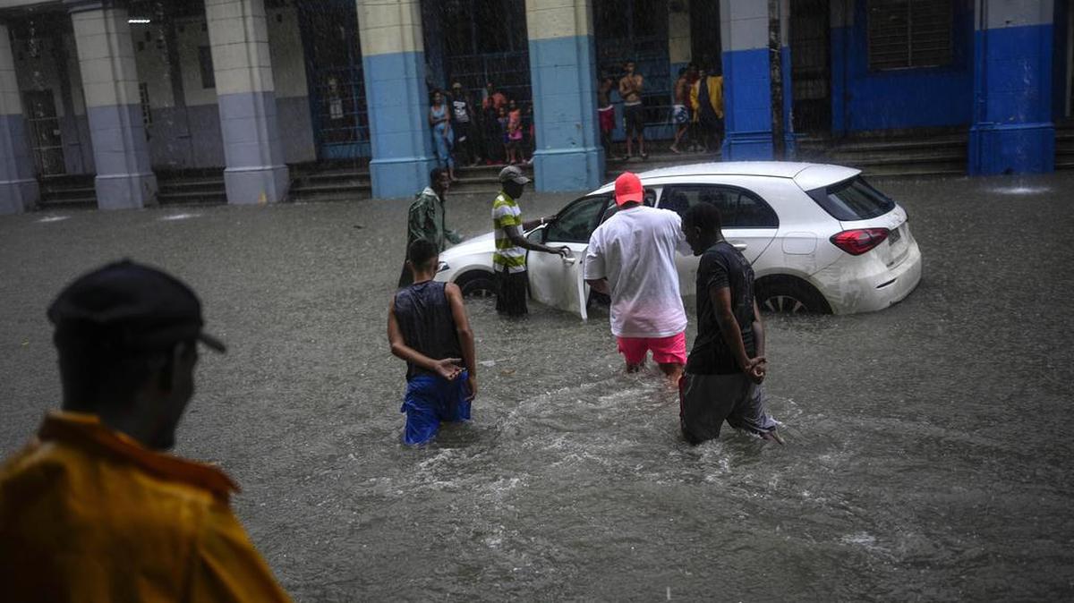 Varias personas acuden a la ayuda de pasajeros de un automóvil, que se detuvo en una calle inundada por fuertes lluvias en La Habana, el viernes 3 de junio del 2022.