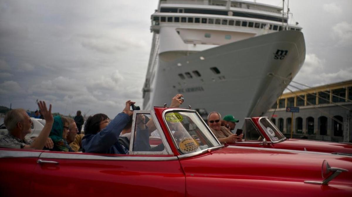 Tourists roll through the Cuban capital in an old car as they pass a cruise ship anchored in Havana Bay on January 17, 2018.