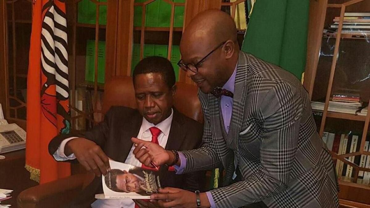 El presidente de Zambia, Edgar Lungu (sentado), recibe una copia del libro Against All Odds de manos del autor Anthony Mukwita.