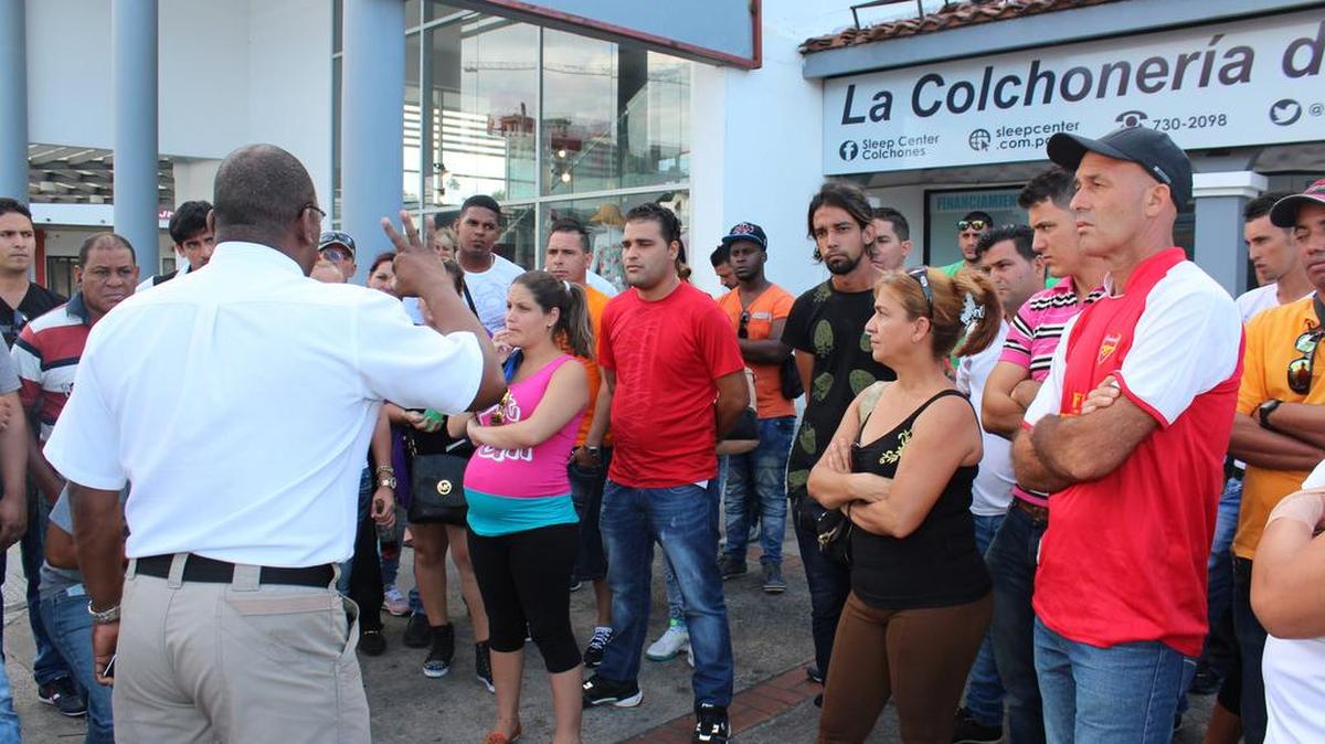 Decenas de cubanos escuchan el 10 de febrero de 2016, en la ciudad de David, capital de la provincia occidental panameña de Chiriquí, a un funcionario de Migración (i) las instrucciones para poder comprar el boleto de avión, por 523,50 dólares cada uno, que les permitirá viajar a México.