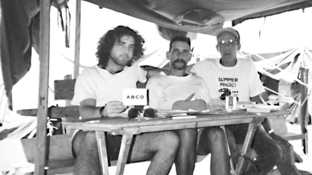 El autor, Gilberto Gutiérrez, con dos balseros alfabetizand., Detalle de mesa de escribir plegable, hecha a partir de un catre de dormir. Campamento Romeo, Guantánamo Bay, 1994.