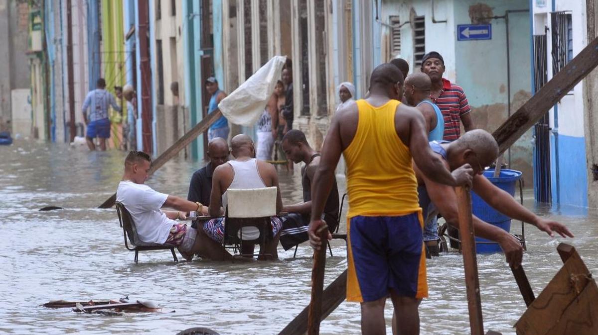En esta foto dada a conocer por el periódico Granma, un grupo de personas juega al dominó en una calle inundada de La Habana, mientras otros tratan de rescatar unos muebles del agua, el 10 de septiembre, después del paso del huracán Irma por la isla.