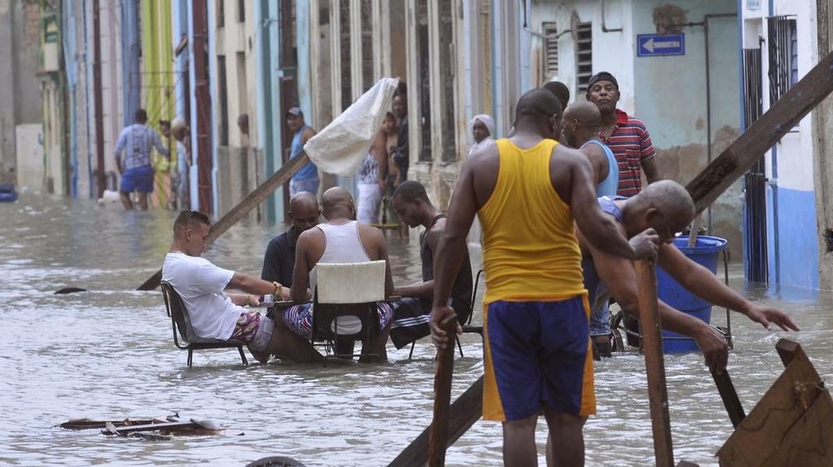 Foto del domingo, 10 de septiembre de 2017, del Granma, muestra a hombres jugando dominó en medio de una calle inundada mientras otros tiran de los muebles destrozados por el agua después del huracán Irma, en La Habana, Cuba.