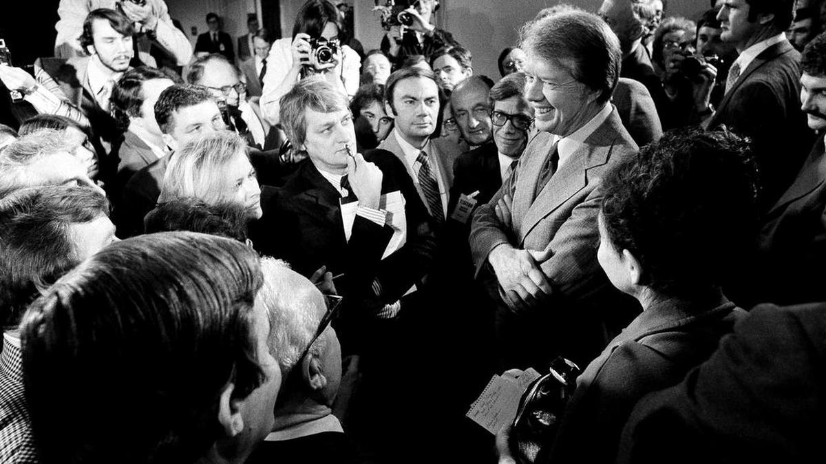 ARCHIVO - En esta foto del 9 de marzo de 1977, el presidente Jimmy Carter, a la derecha, está rodeado de periodistas después de una conferencia de prensa en la que anunció el levantamiento de la prohibición de viajar a Cuba, Vietnam, Corea del Norte y Camboya, en el edificio de oficinas ejecutivo Washington DC.