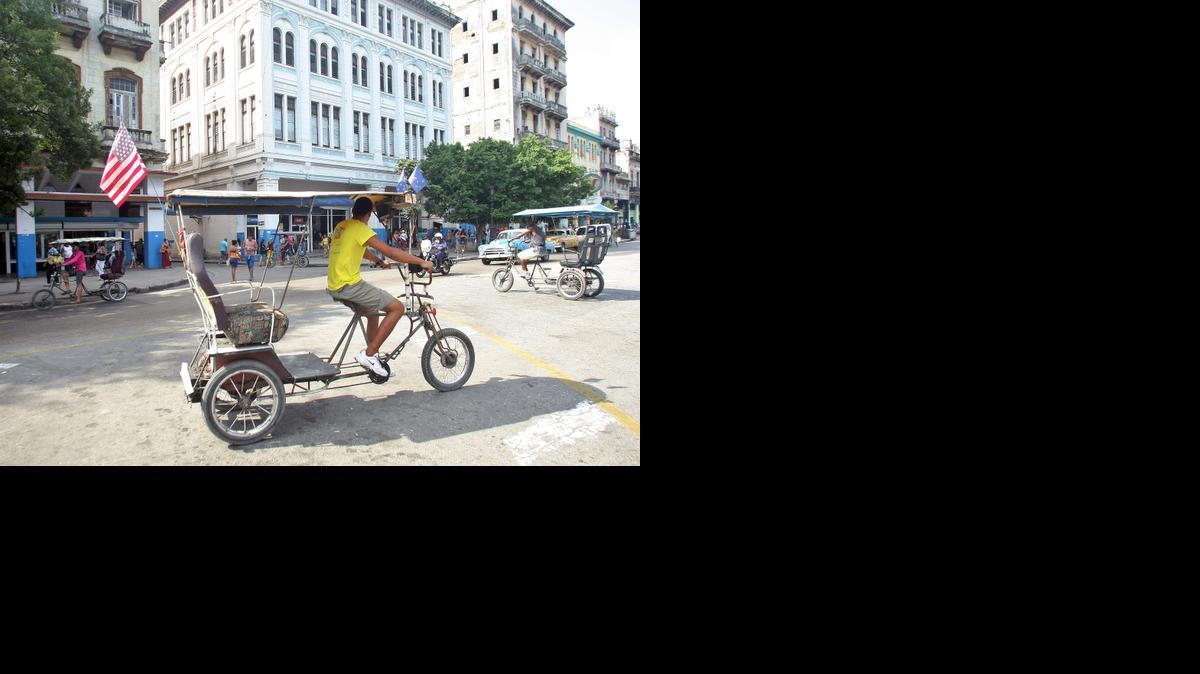 
Un bicitaxista con la bandera de Estados Unidos puesta en su ciclo recorre una calle el domingo 12 de abril del 2015, en La Habana (Cuba). 
