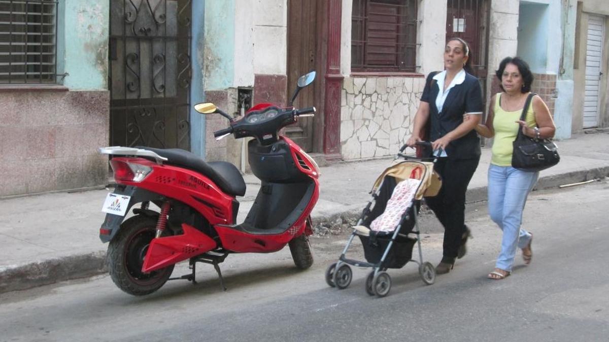 Mujeres caminan en La Habana frente a una motorina estacionada en una calle habanera.