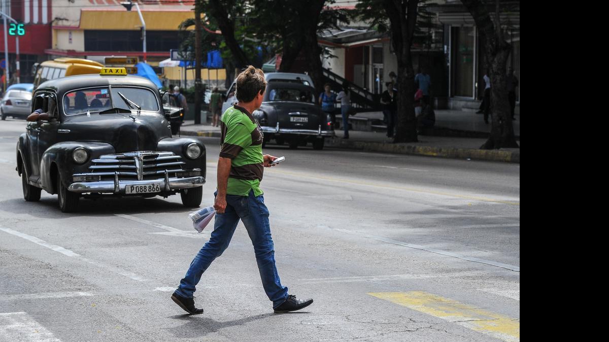 
Un auto museable y hombre usando su teléfono móvil coinciden en una intersección habanera. La atrasada infraestructura tecnológica del país es un impedimento para modernizar las comunicaciones.


