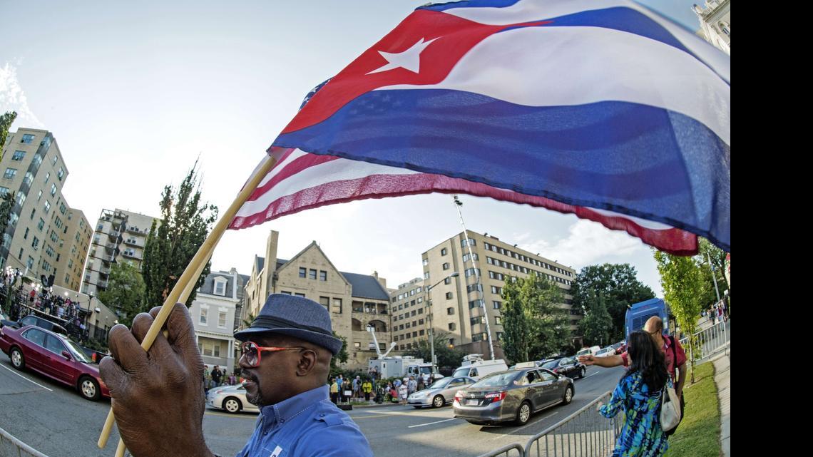 
 Un hombre ondea las banderas de Estados Unidos Y Cuba mientras camina en frente de la nueva Embajada de Cuba poco antes de la ceremonia de apertura oficial del 20 de julio 2015, en Washington, DC. 
