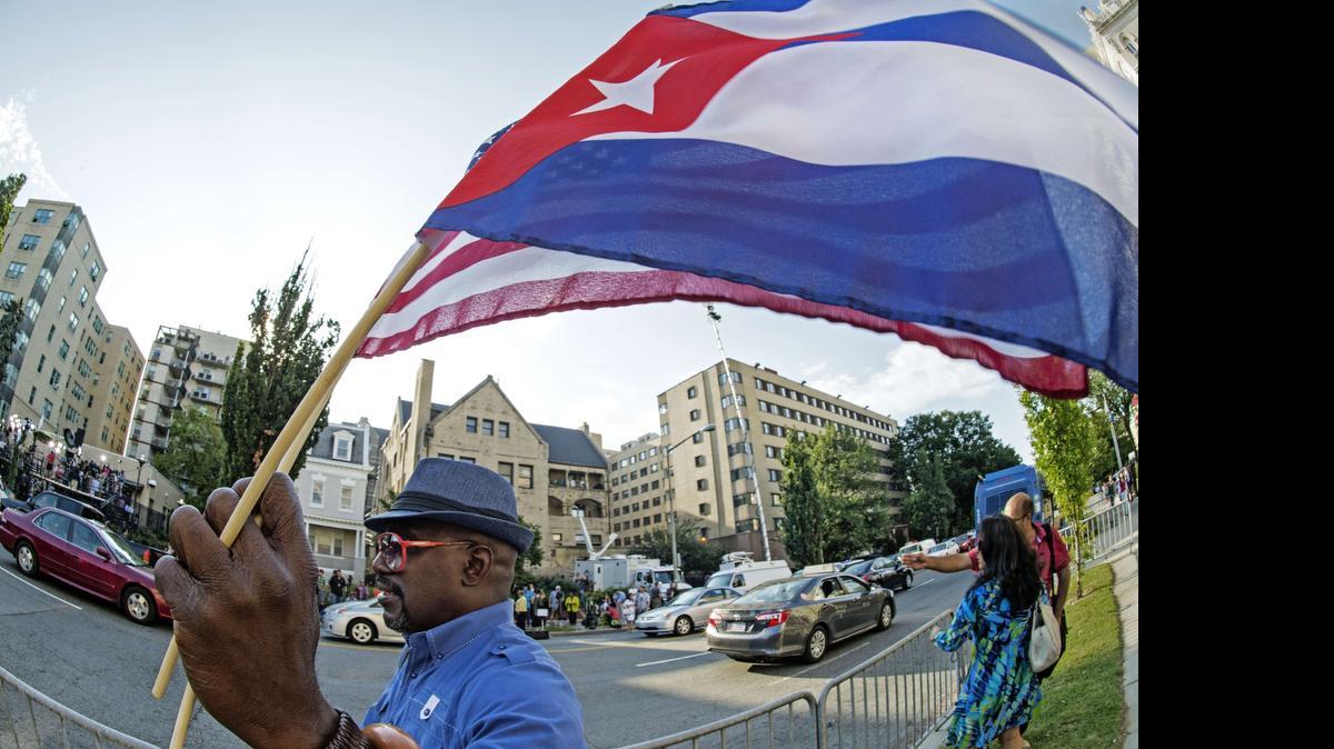 
 Un hombre ondea las banderas de Estados Unidos Y Cuba mientras camina en frente de la nueva Embajada de Cuba poco antes de la ceremonia de apertura oficial del 20 de julio 2015, en Washington, DC. 
