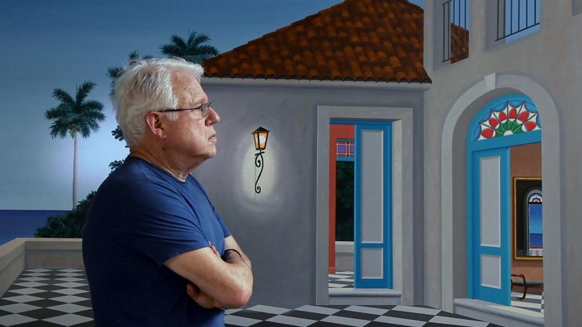 The artist Humberto Calzada in front of one of his paintings, where the house as a background proves the prominence in his work.