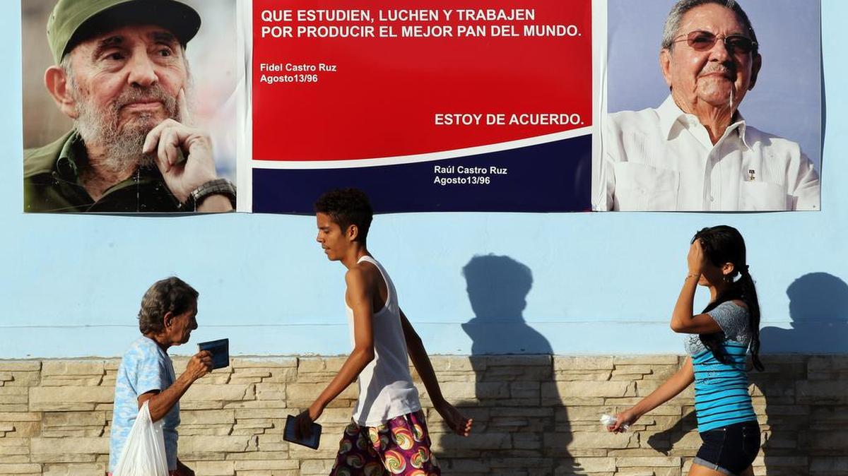Varias persona caminan junto a un cartel con imágenes del líder cubano Fidel Castro y su hermano el gobernante Raúl Castro en La Habana (Cuba) el jueves 17 de diciembre de 2015, al cumplirse el primer aniversario del anuncio del restablecimiento de relaciones entre la isla y EEUU.
