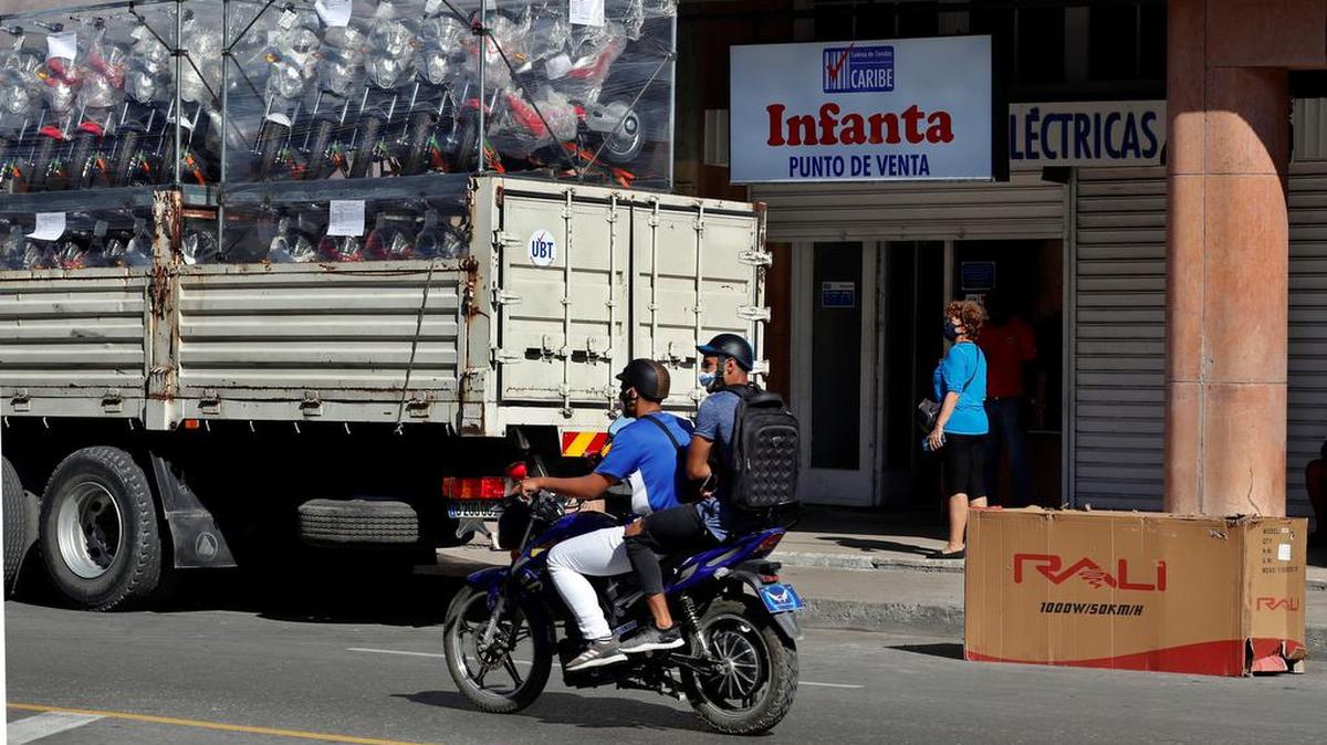Hombres en motocicletas pasan frente a una tienda que vende motocicletas eléctricas en La Habana, Cuba. Los empresarios privados en Cuba hacen malabares para enfrentar los apagones en la isla.