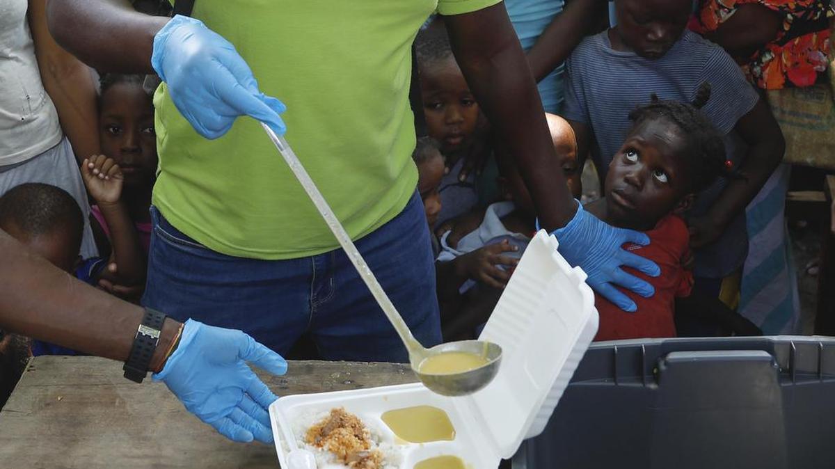 Un camarero sirve sopa en un recipiente mientras los niños hacen fila para recibir comida en un refugio para familias desplazadas por la violencia de las pandillas, en Puerto Príncipe, Haití, el jueves 14 de marzo de 2024.